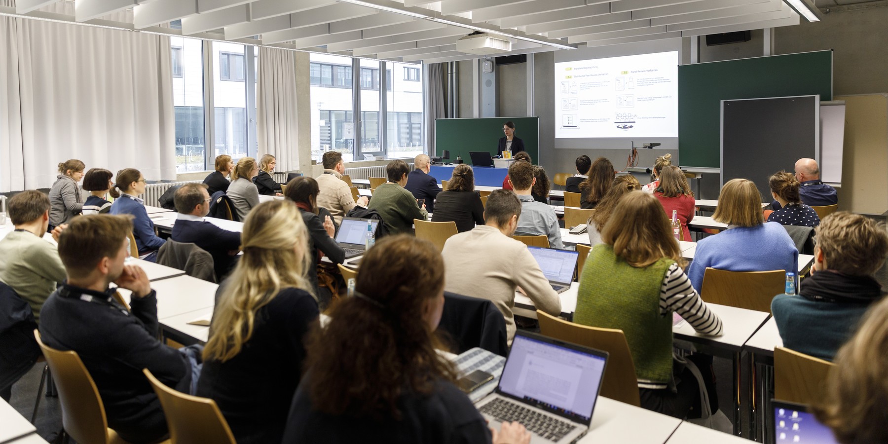 Seminarraum mit Tischreihen, an denen Personen sitzen