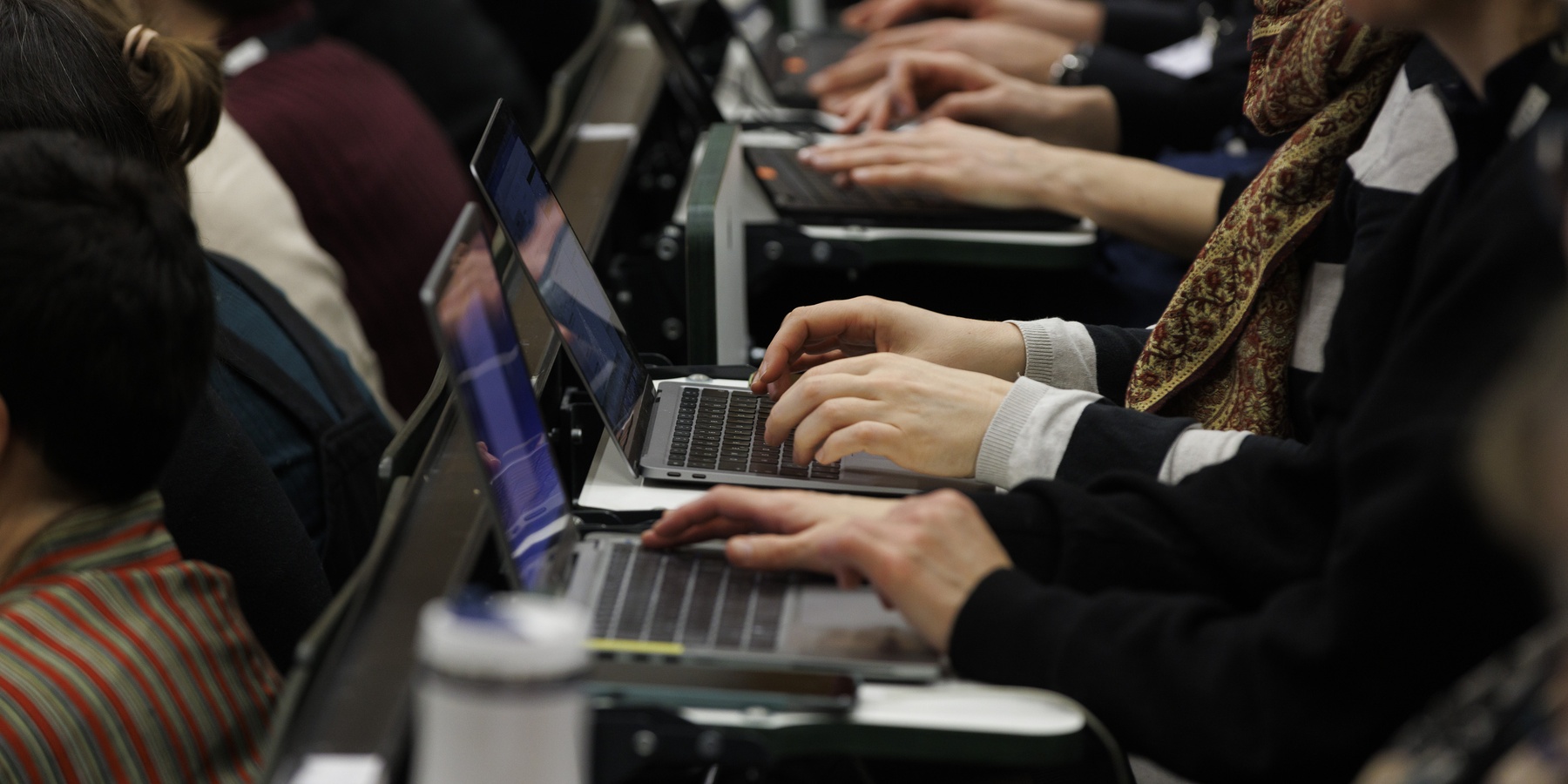 Personen im Hörsaal tippen auf ihren Laptops